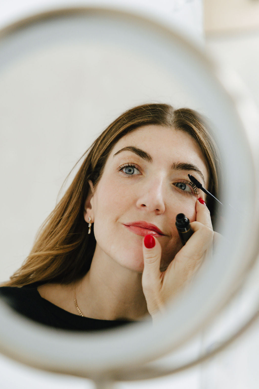 Brunette woman applying Jennifer Lane Beauty's Lane Lashes Mascara in front of a magnifying mirror