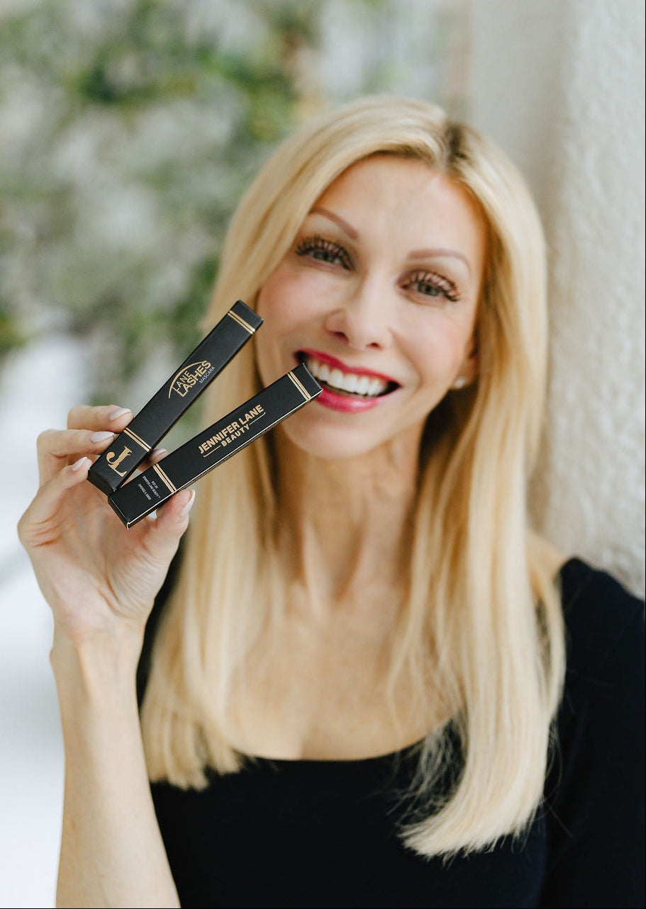 Founder holding two black boxes with brand logos for Jennifer Lane Beauty and Lane Lashes Mascara in gold foill.