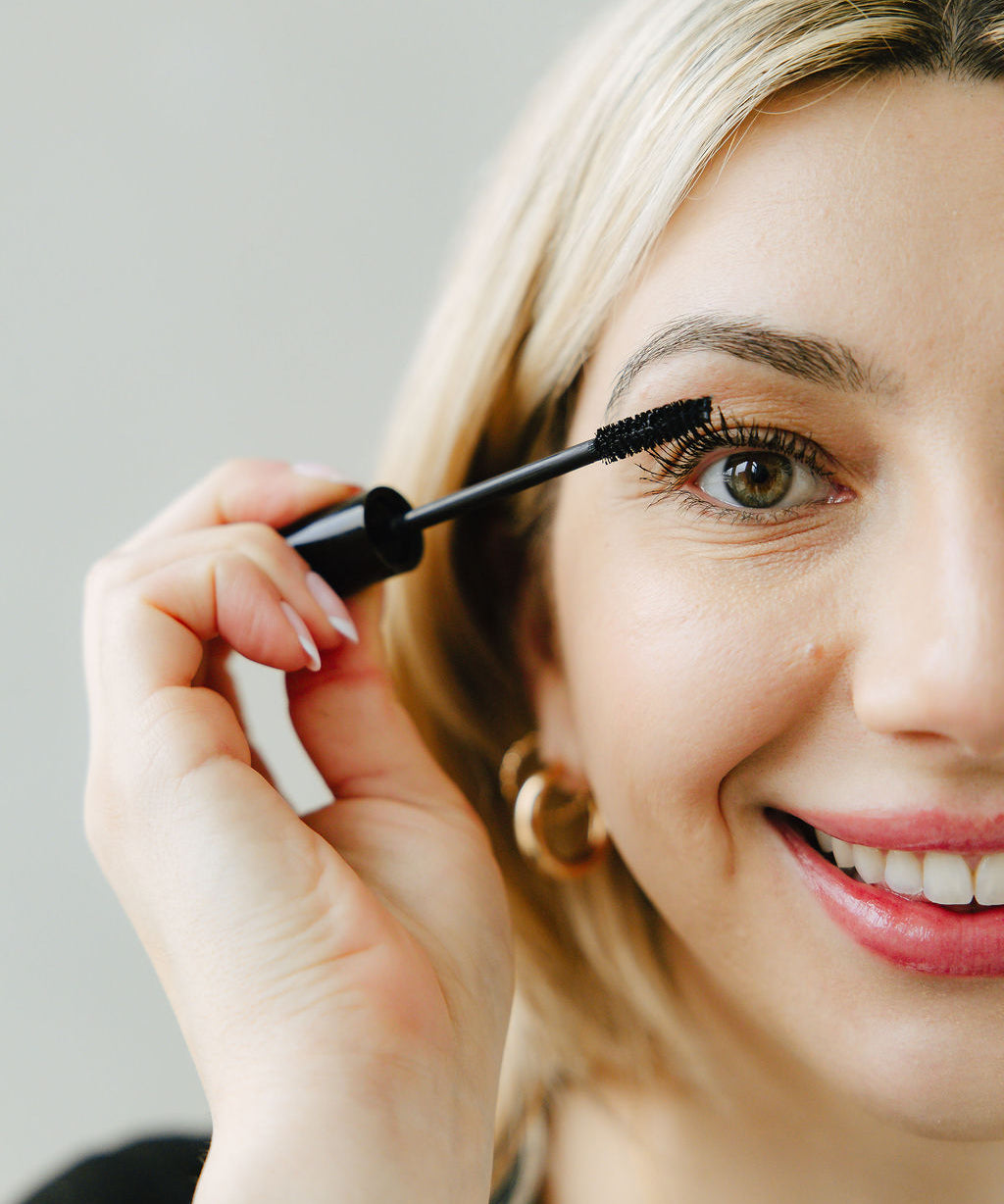 Woman applying Jennifer Lane Beauty's Lane Lashes mascara with a white background
