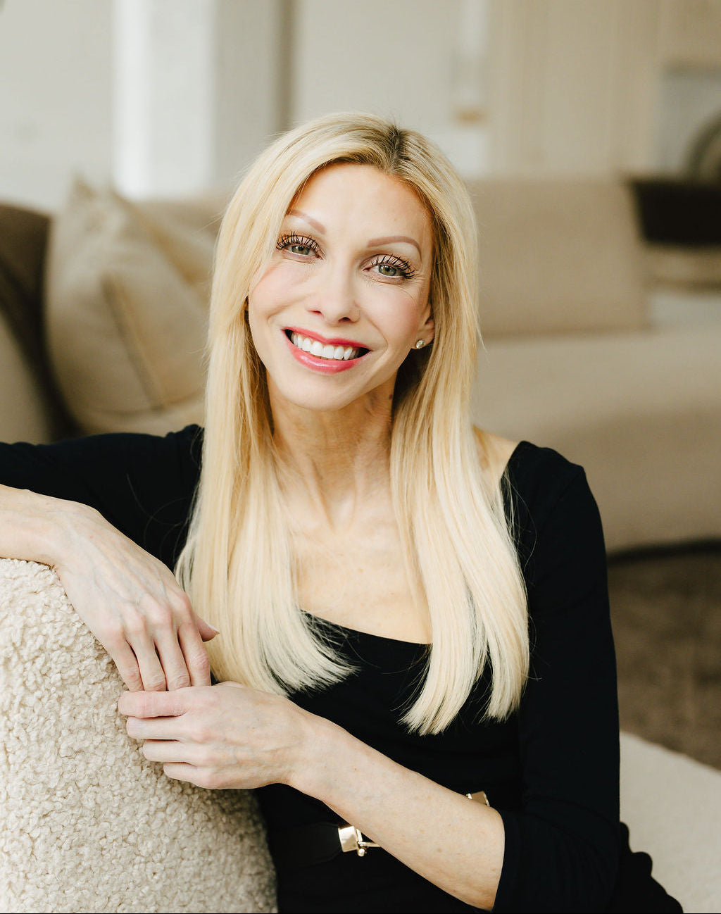 Founder Jennifer Lane with blonde hair and a black top sitting on a couch in a living room.
